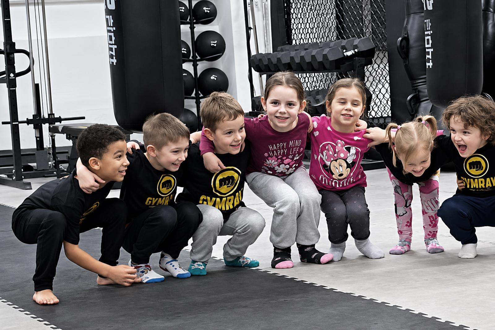 Bambini-Gruppe bei GYMRAY in Bamberg hockt Arm in Arm lachend auf der Matte