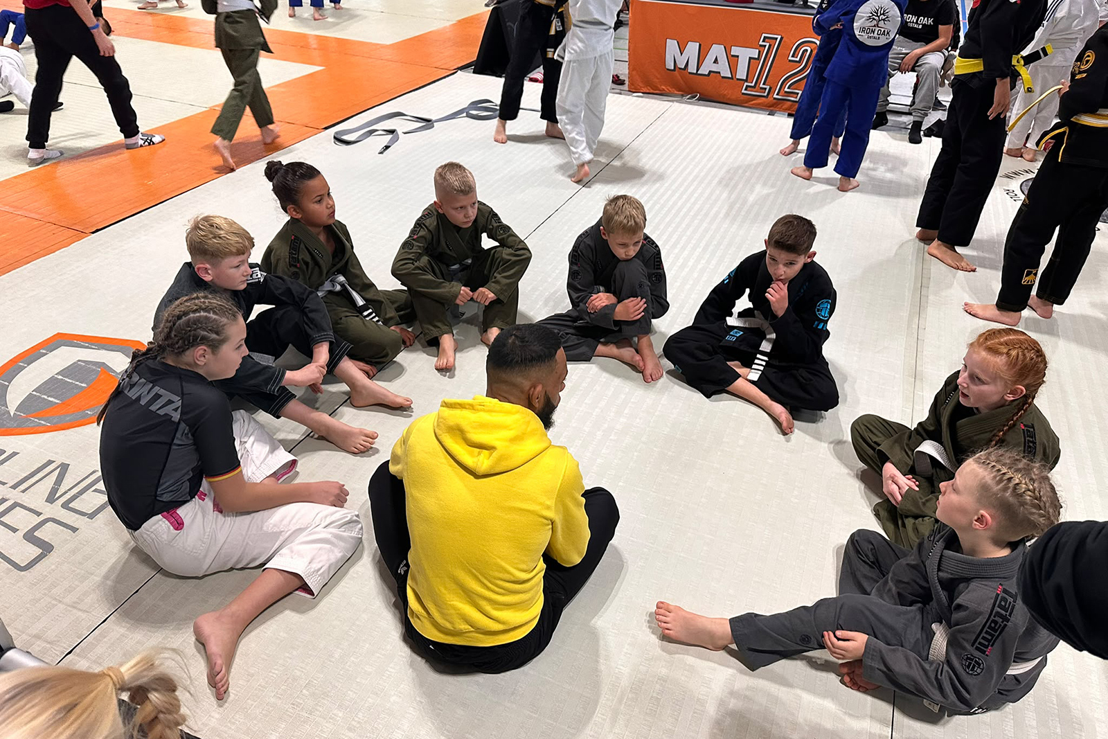 Headcoach Ray sitzt mit den GYMRAY-Nachwuchsathleten im Kreis auf der Matte und bespricht die nächsten Kämpfe bei Grappling Industries Nürnberg